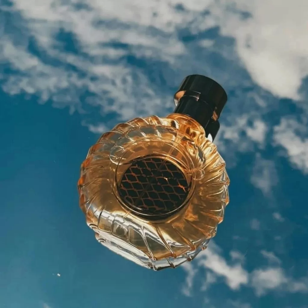 Elegant glass perfume bottle with blue sky and clouds backdrop.